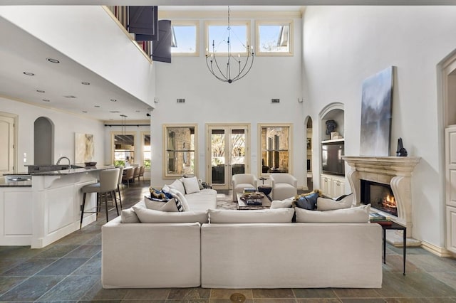 living area with arched walkways, a notable chandelier, recessed lighting, stone finish flooring, and a warm lit fireplace