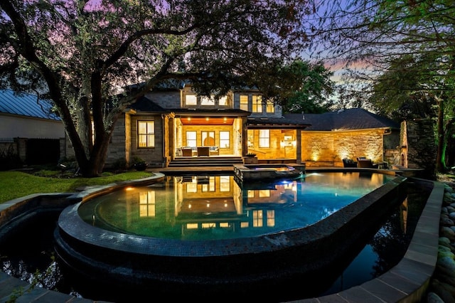 back house at dusk featuring a pool with hot tub