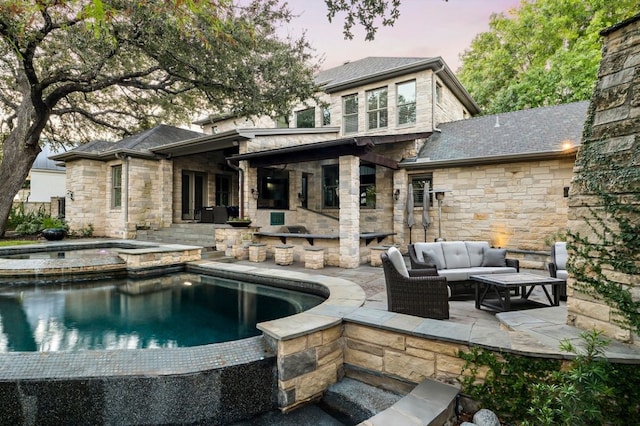 back of property at dusk with an outdoor pool, stone siding, a patio, and an outdoor living space