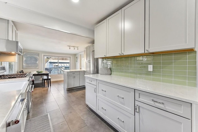 906 E 43rd St, Austin, TX 78751 - kitchen with gas range, decorative backsplash, light tile patterned flooring, white cabinets, and light stone counters