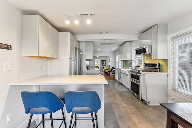 906 E 43rd St, Austin, TX 78751 - kitchen with appliances with stainless steel finishes, a breakfast bar area, light countertops, a peninsula, and decorative backsplash