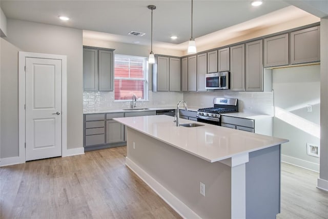 5812 Rotunda Vw, Austin, TX 78747 - kitchen featuring appliances with stainless steel finishes, gray cabinets, light wood-style flooring, a center island with sink, and recessed lighting