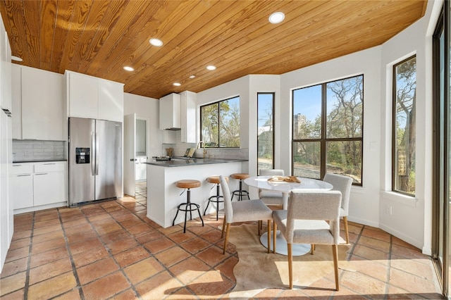 kitchen with stainless steel refrigerator with ice dispenser, wood ceiling, decorative backsplash, and white cabinets