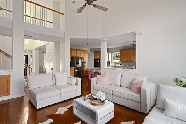 living room with ceiling fan, dark hardwood / wood-style floors, decorative columns, and a high ceiling