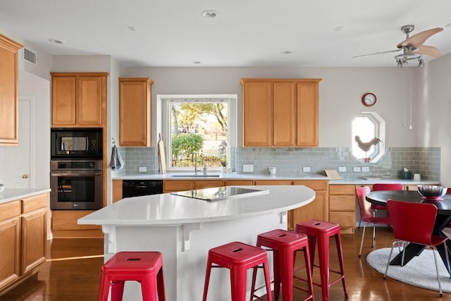 kitchen featuring sink, dark wood-type flooring, a breakfast bar, black appliances, and a kitchen island