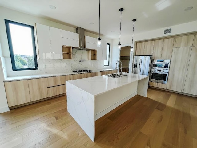 kitchen featuring appliances with stainless steel finishes, pendant lighting, an island with sink, sink, and white cabinets