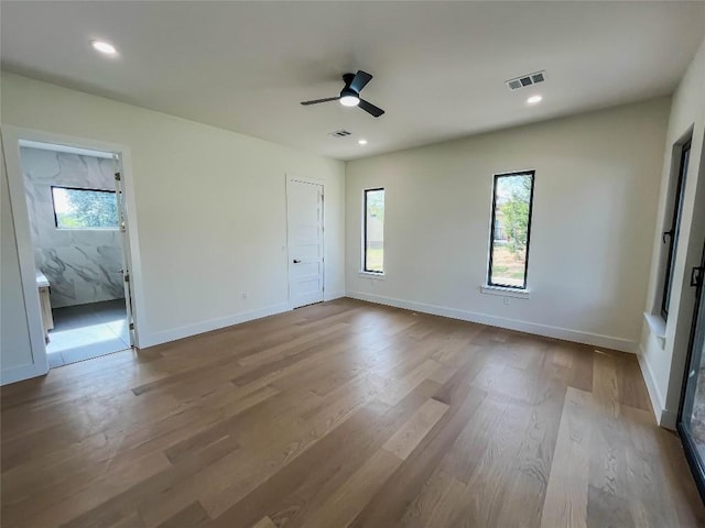 unfurnished bedroom featuring ceiling fan, connected bathroom, multiple windows, and light wood-type flooring