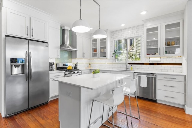 kitchen with sink, appliances with stainless steel finishes, white cabinets, a kitchen island, and wall chimney exhaust hood