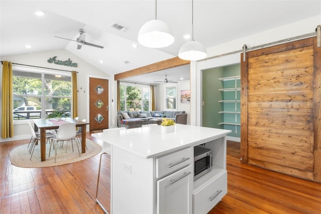 kitchen featuring lofted ceiling, white cabinetry, hanging light fixtures, light hardwood / wood-style floors, and a barn door