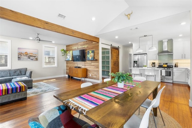 dining room with wooden walls, a barn door, hardwood / wood-style floors, and vaulted ceiling with beams