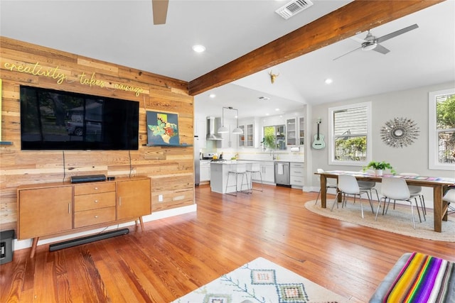 living room with light wood-type flooring, vaulted ceiling with beams, ceiling fan, and wood walls