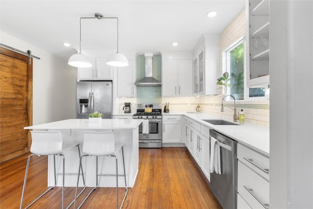 kitchen with wall chimney range hood, sink, appliances with stainless steel finishes, white cabinetry, and a barn door