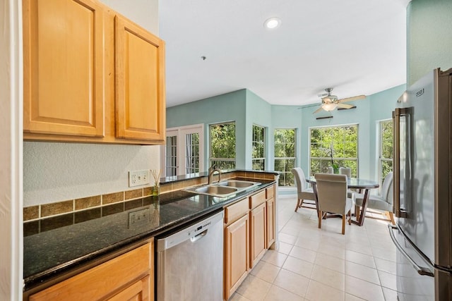 kitchen with appliances with stainless steel finishes, sink, dark stone counters, light tile patterned floors, and ceiling fan