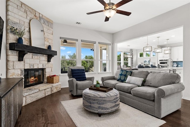 living room with a stone fireplace, dark hardwood / wood-style floors, and ceiling fan