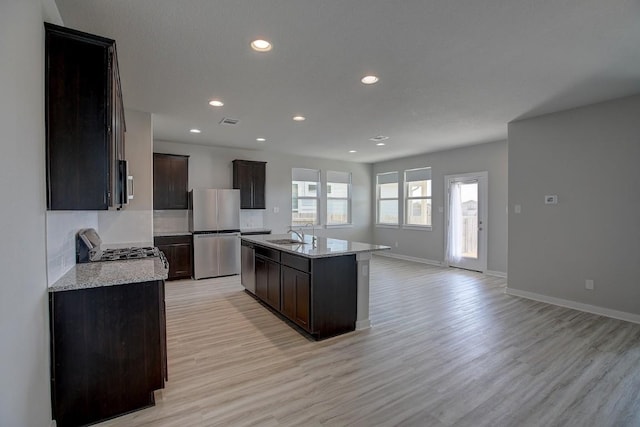 kitchen with light wood finished floors, visible vents, a center island with sink, appliances with stainless steel finishes, and a sink