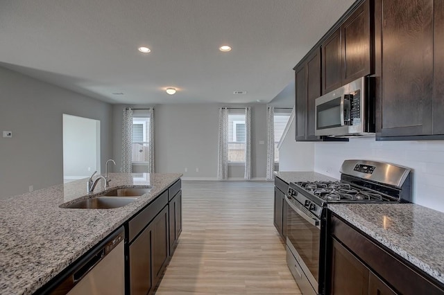 kitchen with a sink, light stone countertops, appliances with stainless steel finishes, and light wood-style flooring