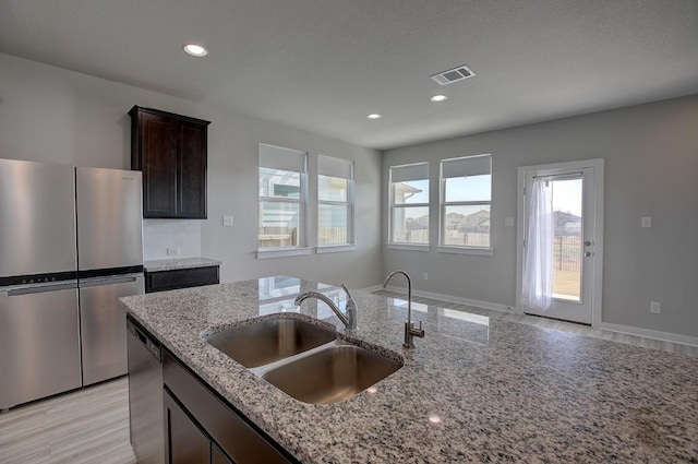 kitchen featuring light stone counters, visible vents, a sink, stainless steel appliances, and dark brown cabinetry