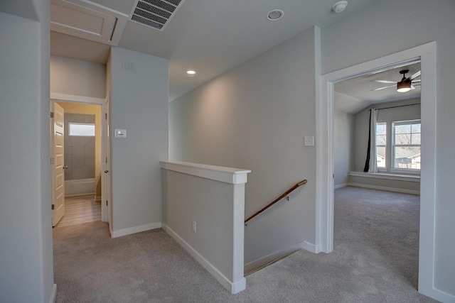 hallway with visible vents, an upstairs landing, carpet, and baseboards