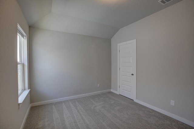 carpeted spare room featuring lofted ceiling and baseboards