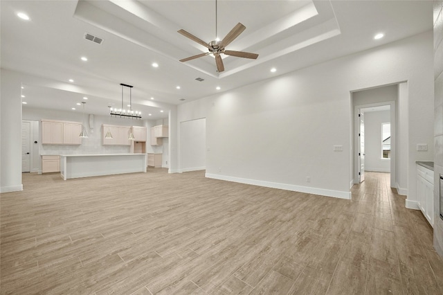 unfurnished living room with ceiling fan, light wood-type flooring, and a tray ceiling