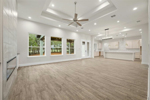 unfurnished living room featuring a tray ceiling, a tiled fireplace, and light hardwood / wood-style flooring