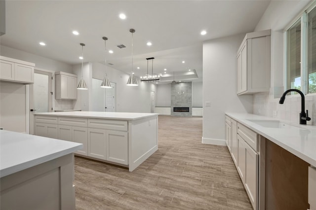 kitchen featuring white cabinetry, sink, decorative light fixtures, and a large fireplace