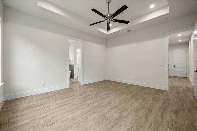 empty room featuring a tray ceiling, light hardwood / wood-style flooring, and ceiling fan