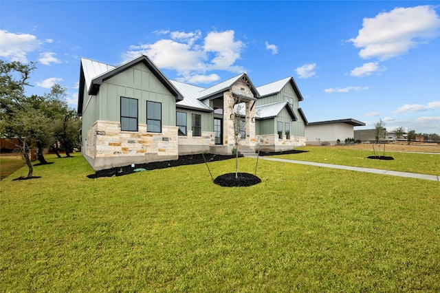 view of front facade with board and batten siding, stone siding, metal roof, and a front lawn