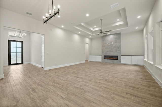 unfurnished living room with a fireplace, a raised ceiling, ceiling fan with notable chandelier, and light wood-type flooring