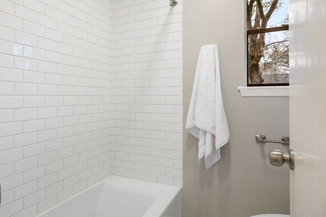 bathroom featuring tiled shower / bath combo and toilet