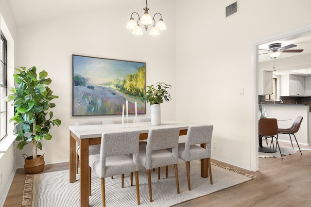 dining space with ceiling fan with notable chandelier and light wood-type flooring