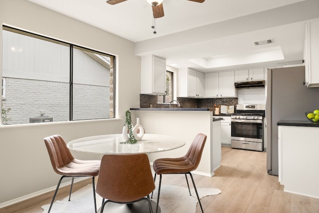 dining room with ceiling fan, a raised ceiling, sink, and light wood-type flooring