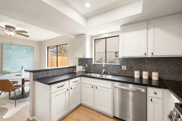 kitchen featuring sink, dishwasher, white cabinetry, backsplash, and a tray ceiling