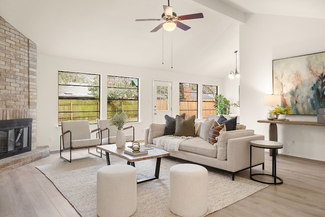 living room featuring ceiling fan with notable chandelier, high vaulted ceiling, a fireplace, light hardwood / wood-style floors, and beam ceiling