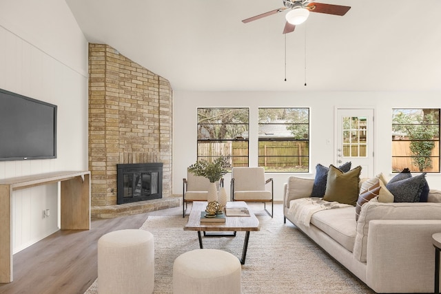 living room featuring ceiling fan, vaulted ceiling, a brick fireplace, and light wood-type flooring