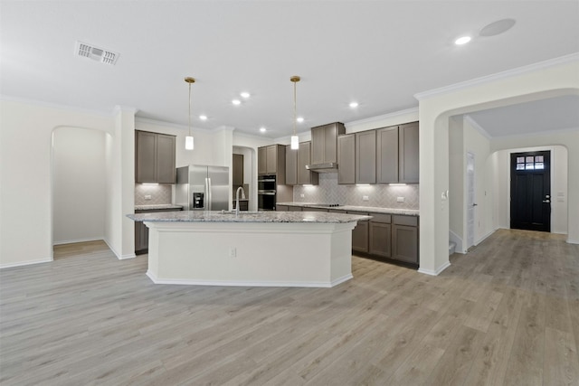 kitchen featuring sink, light stone counters, stainless steel fridge with ice dispenser, a center island with sink, and pendant lighting