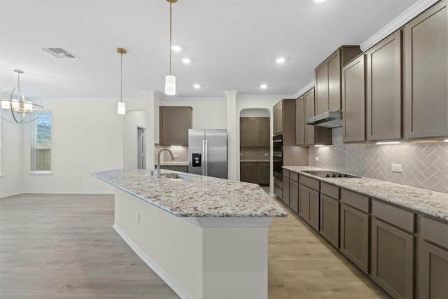 kitchen featuring sink, stainless steel fridge, hanging light fixtures, light stone counters, and a center island with sink