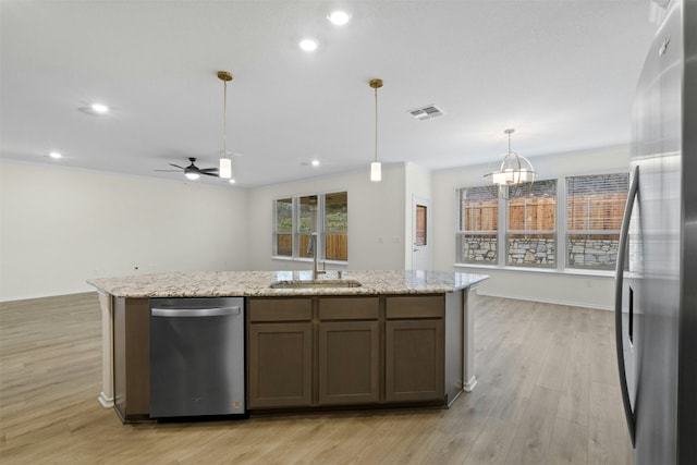 kitchen with sink, light hardwood / wood-style flooring, appliances with stainless steel finishes, light stone countertops, and decorative light fixtures