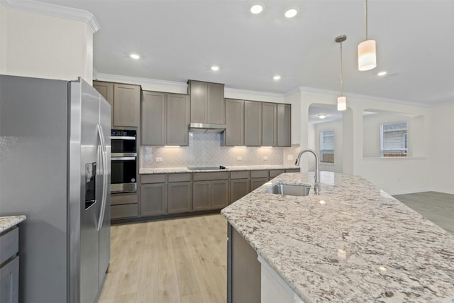 kitchen featuring sink, stainless steel appliances, light stone counters, decorative backsplash, and decorative light fixtures