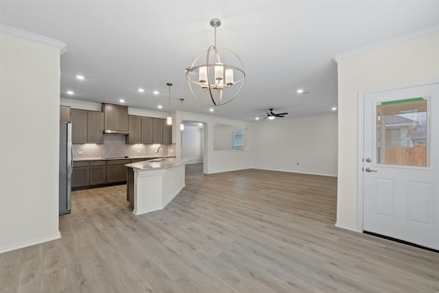 kitchen with light stone counters, crown molding, decorative light fixtures, a center island with sink, and stainless steel fridge