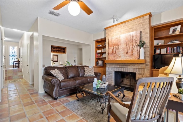 living room featuring light tile patterned flooring, built in features, a fireplace, ceiling fan, and a textured ceiling