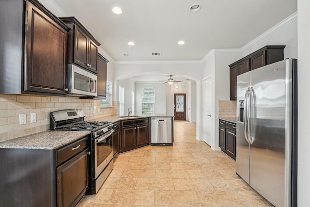 kitchen featuring dark brown cabinetry, crown molding, kitchen peninsula, stainless steel appliances, and backsplash