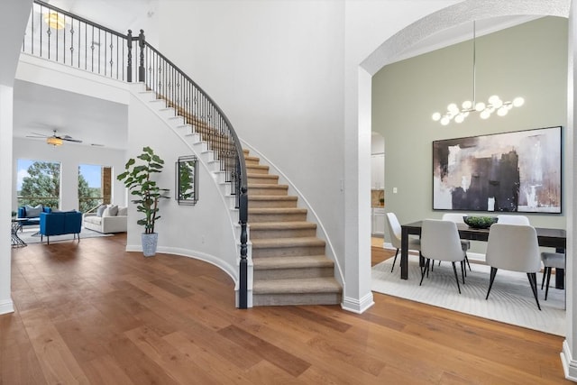 stairs with a towering ceiling, wood-type flooring, and ceiling fan with notable chandelier