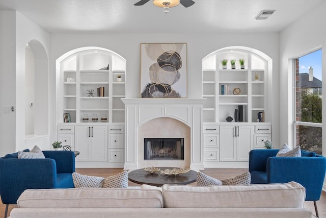 living room featuring light hardwood / wood-style flooring, built in features, a premium fireplace, and ceiling fan