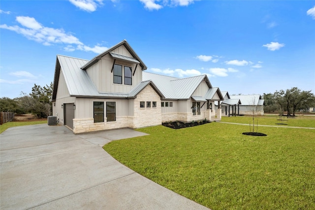 view of front facade with central air condition unit, concrete driveway, a front yard, metal roof, and stone siding