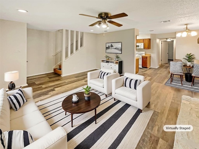 living room with ceiling fan with notable chandelier, light wood-type flooring, and a textured ceiling