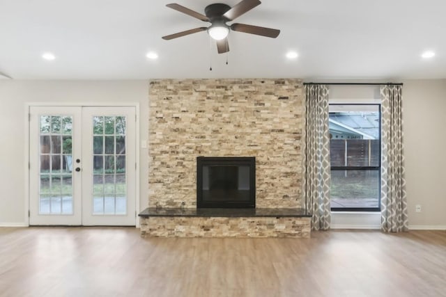 unfurnished living room featuring french doors, a large fireplace, a healthy amount of sunlight, and wood-type flooring