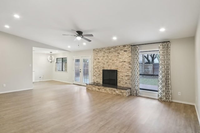 unfurnished living room with ceiling fan with notable chandelier, a fireplace, wood-type flooring, lofted ceiling, and french doors