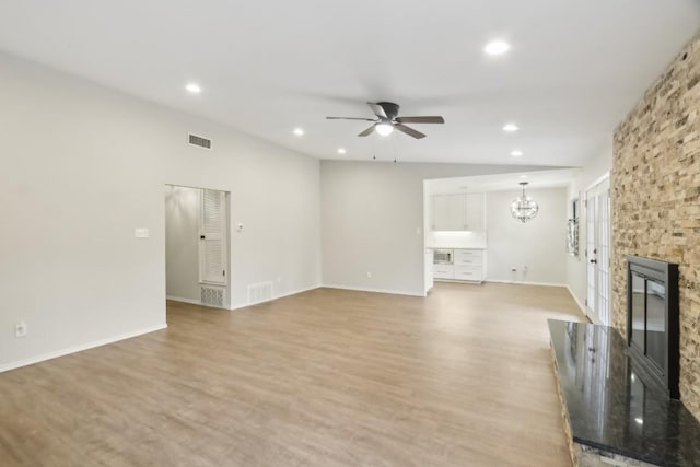 unfurnished living room featuring a stone fireplace, ceiling fan with notable chandelier, and light wood-type flooring