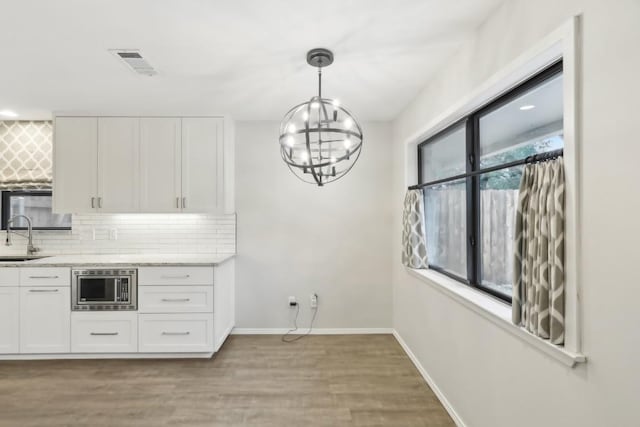 kitchen with stainless steel microwave, decorative light fixtures, sink, white cabinets, and decorative backsplash